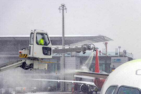 Ground crew spraying de-icing fluid onto the tail wing of an aircraft during winter operations