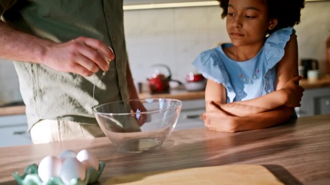 Sad daughter crossing arms watching father crack eggs. Family breakfast kitchen.