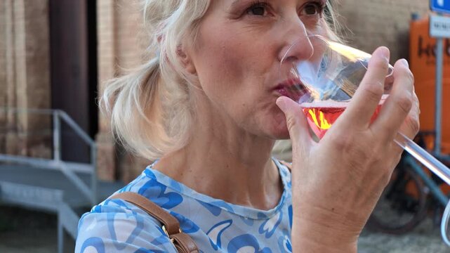 Blonde woman savoring the aroma of Lambrusco rose wine in a glass at a lively Castelvetro tasting festival, enjoying local Emilia-Romagna wine culture and tradition in Italy. SLOW MOTION