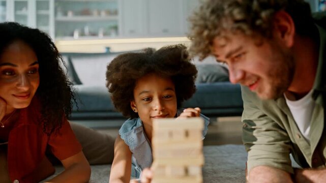 Daughter stacking wooden tower parents. Family board game living room floor.