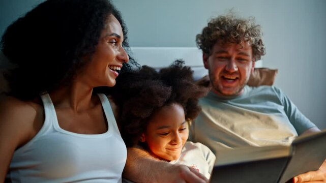 Parents reading bedtime story daughter bed. Multiracial family evening book.