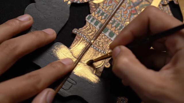 Craftsman painting intricate golden patterns on traditional shadow puppet
