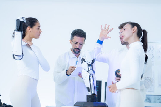 Robotics demonstration day: an engineer fans out his own fingers beside a raised bionic arm, giving the team a human yardstick for the machine hand held above them