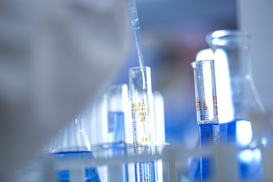 The gloved hands of a medical research scientist dripping solution into the graduated cylinder inside a clean pharmaceutical research laboratory, in a clean and modern laboratory.