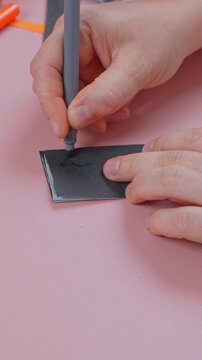 Fingers hold a soft tip pen and sketch a jagged line across a small stack of folded black paper on a pink surface, a simple step by step method for repeating cutout shapes.