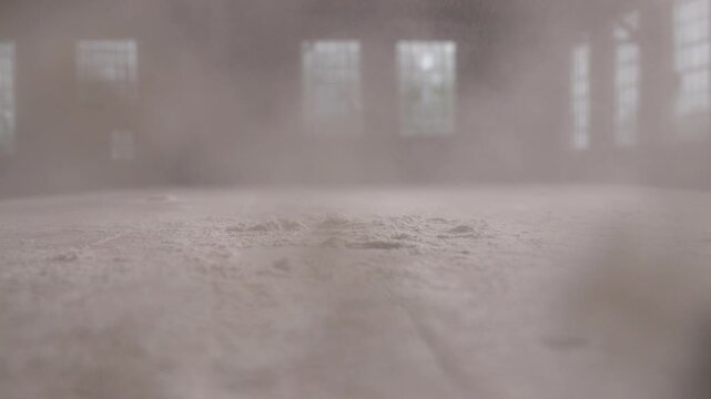 Dust erupts from a table in an old warehouse, creating a dramatic atmosphere due to slap of hand.
