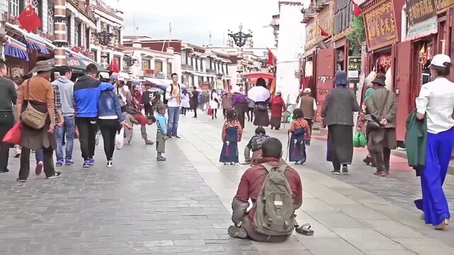 Buddhist pilgrims and tourists walking along a traditional stone-paved street in Lhasa, Tibet, with monks prostrating and locals in ethnic dress