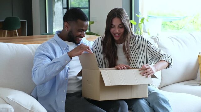 Couple opens a delivery package at home, then laughs and smiles with surprise while looking inside. Their happy unboxing reaction supports online shopping, ecommerce, shipping and home delivery.