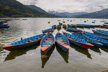 Colorful wooden boats floating on the calm waters of Phewa Lake in Pokhara, Nepal, surrounded by lush green hills and the dramatic Himalayan landscape of the Annapurna region © Yuliia
