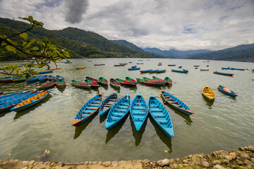 Colorful wooden boats floating on the calm waters of Phewa Lake in Pokhara, Nepal, surrounded by lush green hills and the dramatic Himalayan landscape of the Annapurna region © Yuliia