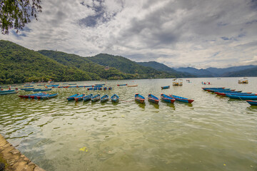 Colorful wooden boats floating on the calm waters of Phewa Lake in Pokhara, Nepal, surrounded by lush green hills and the dramatic Himalayan landscape of the Annapurna region © Yuliia