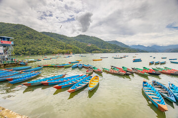 Colorful wooden boats floating on the calm waters of Phewa Lake in Pokhara, Nepal, surrounded by lush green hills and the dramatic Himalayan landscape of the Annapurna region © Yuliia