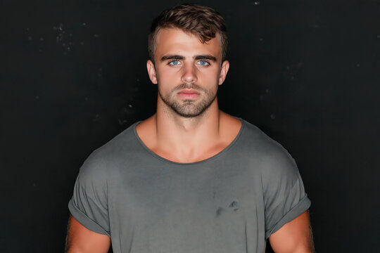 Athletic young man wearing gray shirt against dark studio background