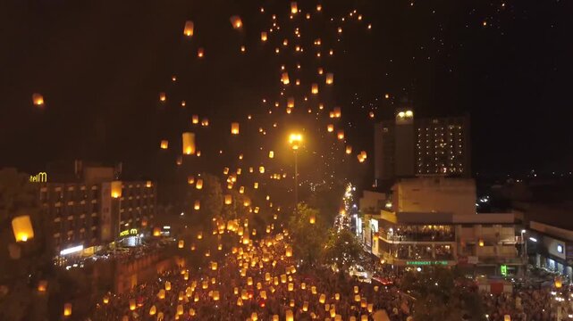 Thousands of glowing sky lanterns ascending over a packed city street at night during a cultural festival