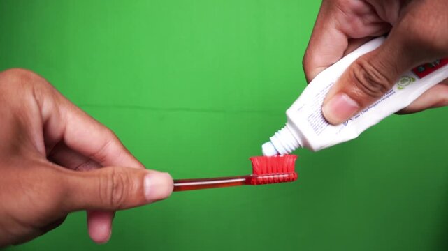 Close Up of Hands Squeezing White Toothpaste from Tube onto Red Toothbrush on Green Screen Chroma Key