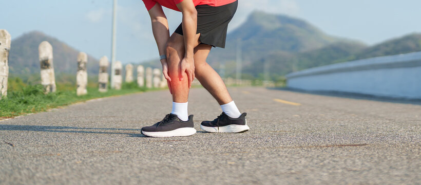 Young adult man runner suffering from acute calf muscle pull and leg ache during running workout. Male athlete holding his painful leg due to sports injuries. Medical and healthcare concept