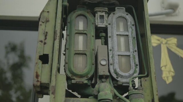 Close-up of two vertical sight-glass flow meters and connected pipes mounted in a chipped green metal housing, showing corrosion, grime and visible gallon markings.