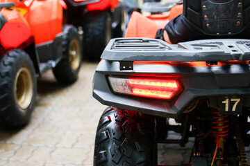 All terrain vehicle with glowing rear light and rugged tire parked beside red quad bike on paved outdoor ground, conveying adventure and recreational travel © CoreRock