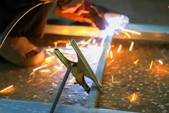 Metal worker welding steel frame with bright sparks in workshop, creating dramatic industrial scene with protective equipment and glowing light