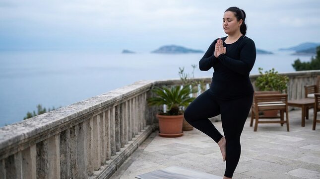 Woman practicing yoga tree pose on balcony overlooking the sea