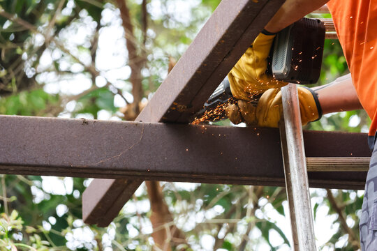 Worker cutting steel beam with power saw, sparks flying during outdoor construction work in forested setting
