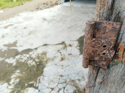 Rusty old metal door hinge nailed on weathered wooden post with cracked concrete