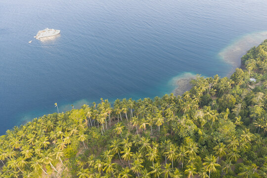 A small ship cruises along the scenic coast of Makian Island, a volcano just south of Ternate near Halmahera, Indonesia. The coral reefs of this region support extraordinary marine biodiversity.