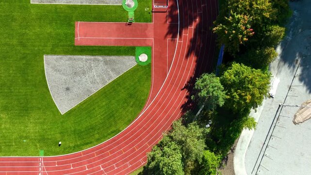 Cinematic aerial topdown shot of a professional sports stadium featuring a red running track and green grass field. Ideal for fitness, wellness, and competition concepts.