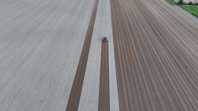 Tractor seeding precisely aligned rows across prepared agricultural fields, parallel furrows, precision farming, Po Valley farmland, drone tracking