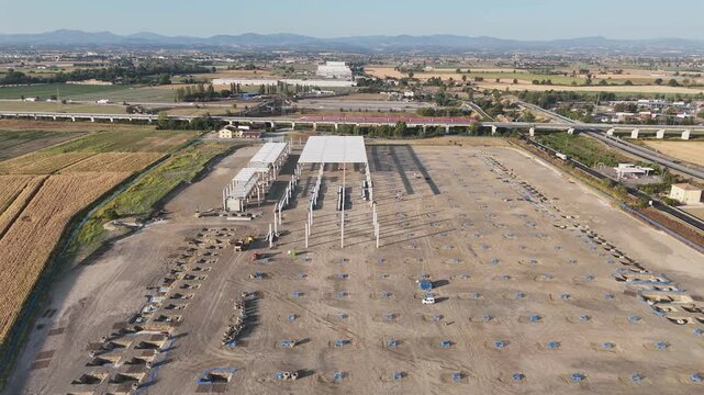 Large logistics facility under construction, steel warehouse frames, concrete foundations, structural columns, construction equipment and transport infrastructure, drone forward flyover.