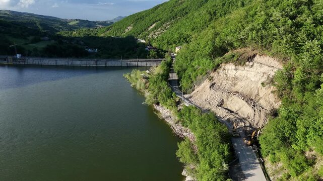 Lake Mignano borders a fresh landslide scar and exposed road cut beside SP21, documenting slope failure, rockfall and erosion within the sedimentary Arda Valley during a drone slide.