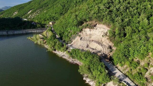 Lake Mignano borders a major landslide scar beside SP21, exposing disturbed sedimentary terrain and slope failure deposits near the reservoir during an aerial slide.