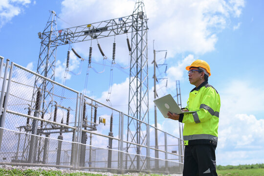 Electrical engineer, safety helmet, laptop, electrical substation, power transmission, industrial worker inspecting equipment under bright blue sky