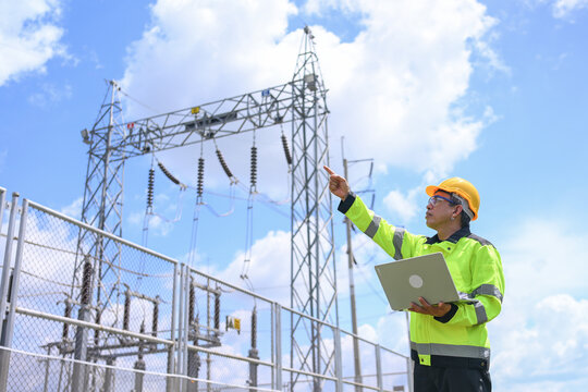Electrical engineer inspecting power substation equipment beneath bright blue sky, conveying technical focus and workplace safety during outdoor grid maintenance operations