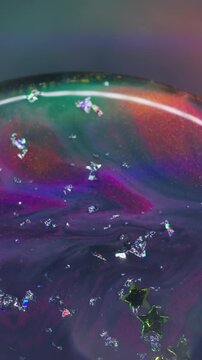 Vertical video. Ink spill. Light stars texture. Defocused purple blue yellow color golden crystal liquid floating on abstract neon bokeh background.