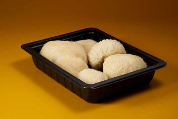 Fresh Lion's Mane mushrooms, Hericium erinaceus, arranged in a black food tray on a warm background, highlighting their distinctive white spiny texture and culinary appeal. © DEWINs