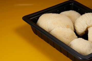 Close-up of fresh Hericium erinaceus mushrooms arranged in a black tray, emphasizing their delicate white spines and natural texture against a warm orange background. © DEWINs