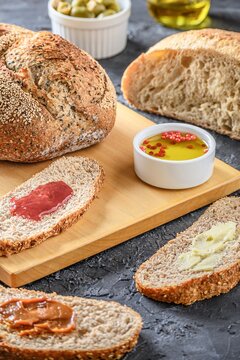 Artisan whole grain bread served with butter, jam, peanut butter, and olive oil with pink peppercorns &mdash; rustic flat lay on dark stone background for food blogs, bakeries, or healthy lifestyle branding