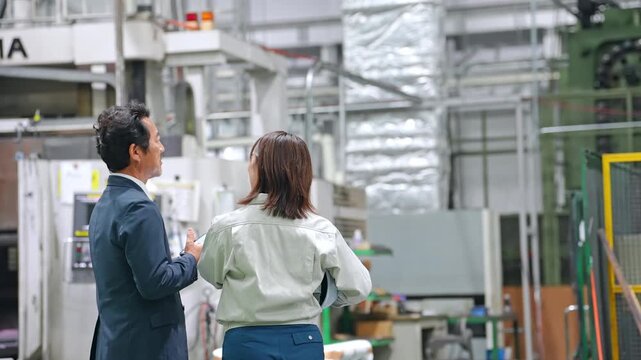 A male businessperson and a female factory worker inspecting a factory.