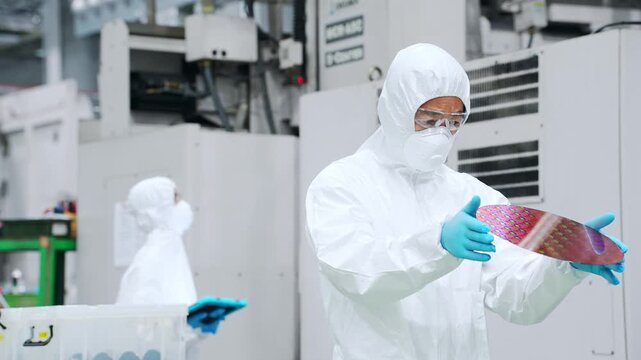 半導体工場でシリコンウエハーを検査する防塵服を着た男性作業員