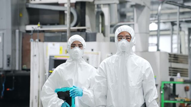 Male and female workers in protective suits standing in a factory