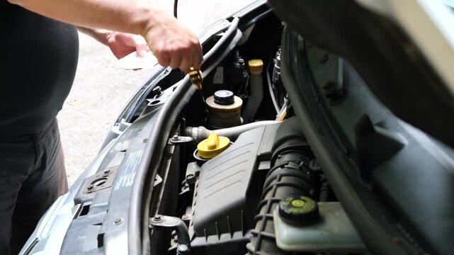 Close view of a driver checking the engine oil level with a dipstick during routine vehicle maintenance