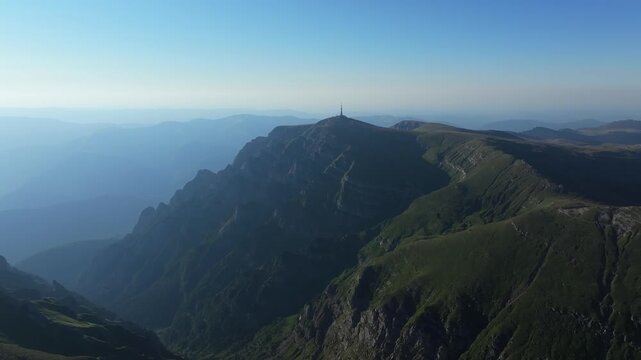 A high-altitude wide drone shot showing Costila peak and its iconic communication tower among the rugged ridges of Bucegi mountains, Romania