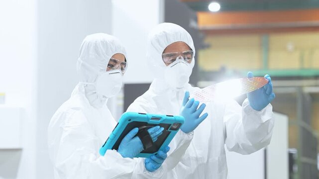 半導体工場でタブレットを持ってシリコンウエハーを検査する防護服を着た男女作業員