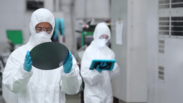 半導体工場でシリコンウエハーを検査する防護服を着た男性作業員