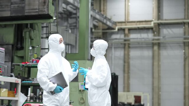 Male and female workers in protective suits converse inside the factory.