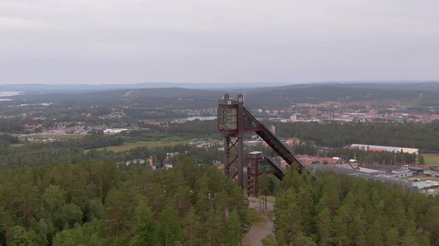 Aerial drone flyover toward Lugnet ski jump tower, Falun, Sweden, hazy summer.