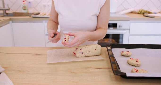 Cookies recipe. Baker work. Woman hand cut biscotti roll log dough with cranberry on home kitchen table placing treat on oven tray.