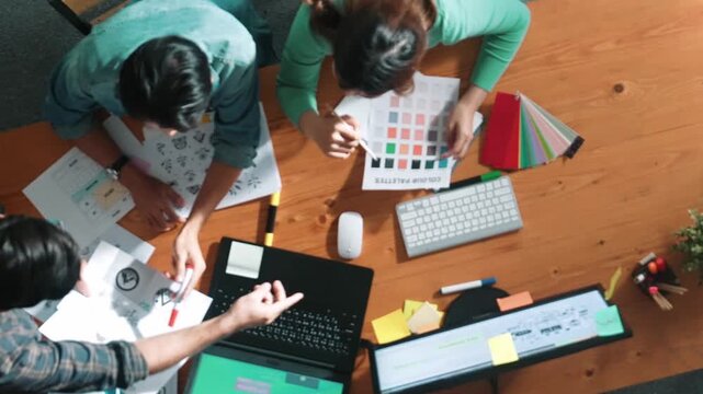 Top view of project manager writing idea while team joining meeting and talking about idea. Professional designer design logo while looking at color palette and writing idea down in paper. Symposium.
