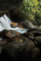 Vertical framing of a waterfall viewed from beneath a dark rocky shelter, surrounded by dense green bamboo and lush rainforest foliage. © k33pcalmncapture